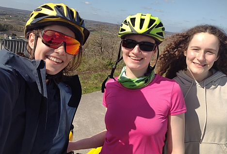 Drei Personen mit Fahrradhelmen machen ein Selfie bei sonnigem Wetter und blauem Himmel