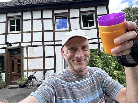 Mann mit bunten Plastikbechern vor Fachwerkhaus