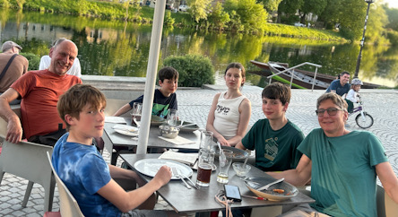 Mehrere Personen sitzen an einem Tisch im Außenbereich eines Restaurants am Flussufer