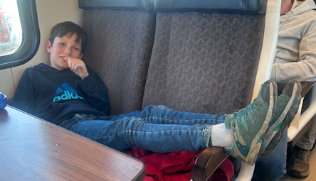 Kind sitzt mit ausgestreckten Beinen auf einem Sitzplatz in einem Zugabteil