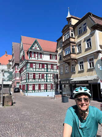 Person mit Fahrradhelm steht mit Fahrrad auf einem Marktplatz mit historischen Fachwerkhäusern