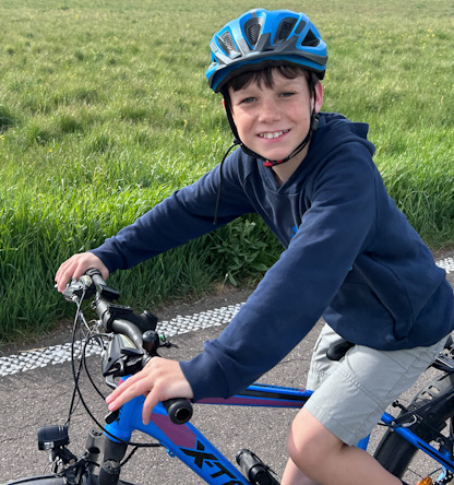 Kind mit Fahrradhelm fährt auf einem asphaltierten Weg entlang einer grünen Wiese