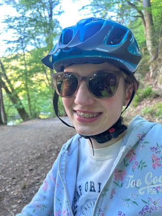 Nahaufnahme einer Person mit Fahrradhelm und Sonnenbrille auf einem Waldweg