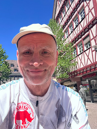 Person mit Fahrradtrikot und Kappe steht in einer Altstadt mit Fachwerkhäusern
