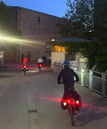 Mehrere Kinder fahren in der Dämmerung mit beleuchteten Fahrrädern über eine Brücke