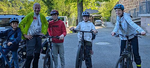 Gruppe von Erwachsenen und Kindern mit Fahrrädern steht auf einem Parkplatz vor einem Gebäude