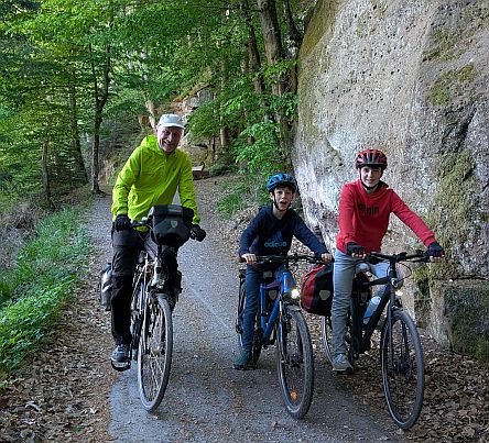 Vier Personen fahren mit Fahrrädern auf einem schmalen Weg durch eine felsige Waldschlucht